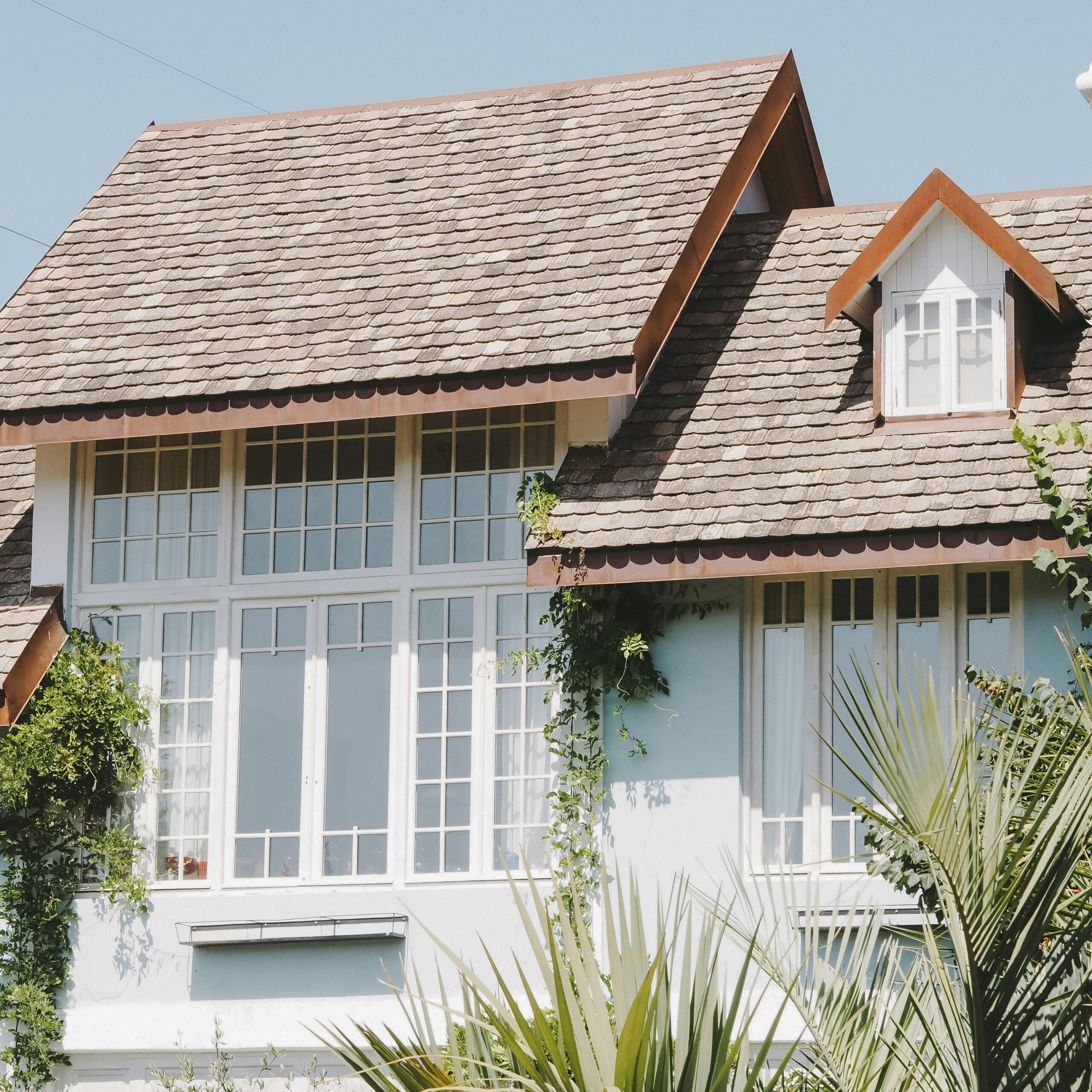 Elegant suburban house with large windows and a shingled slate roof in sunlight.