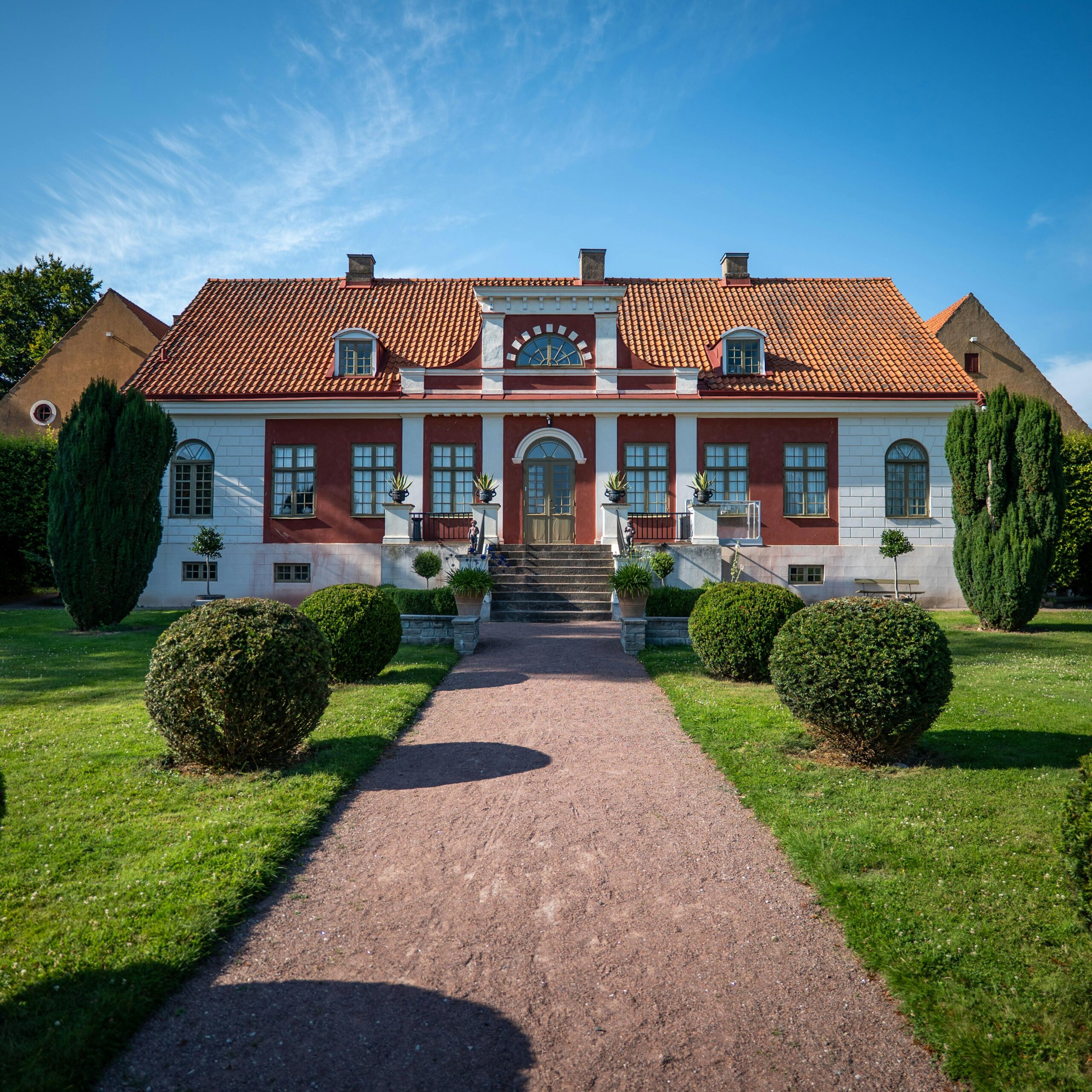Beautiful historic mansion in Skåne, Sweden, surrounded by lush green gardens under a clear summer sky.